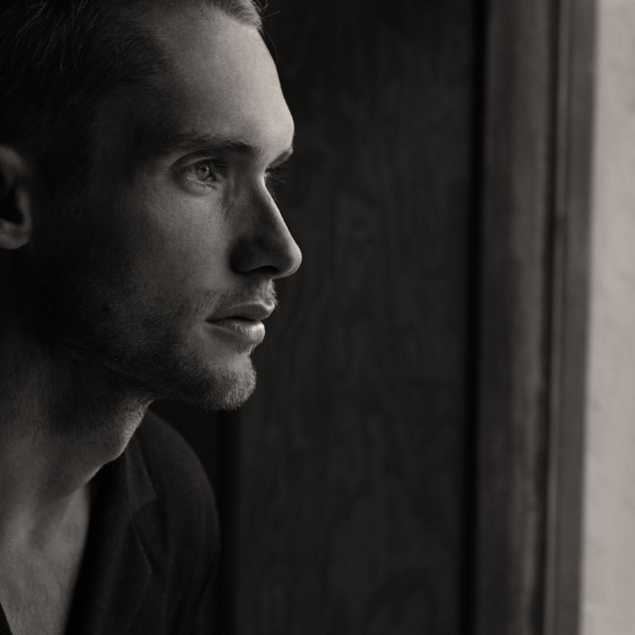 Black and White image of a young man staring out a window