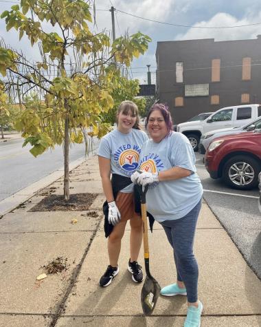 two ladies standing on a side walk with a shovel