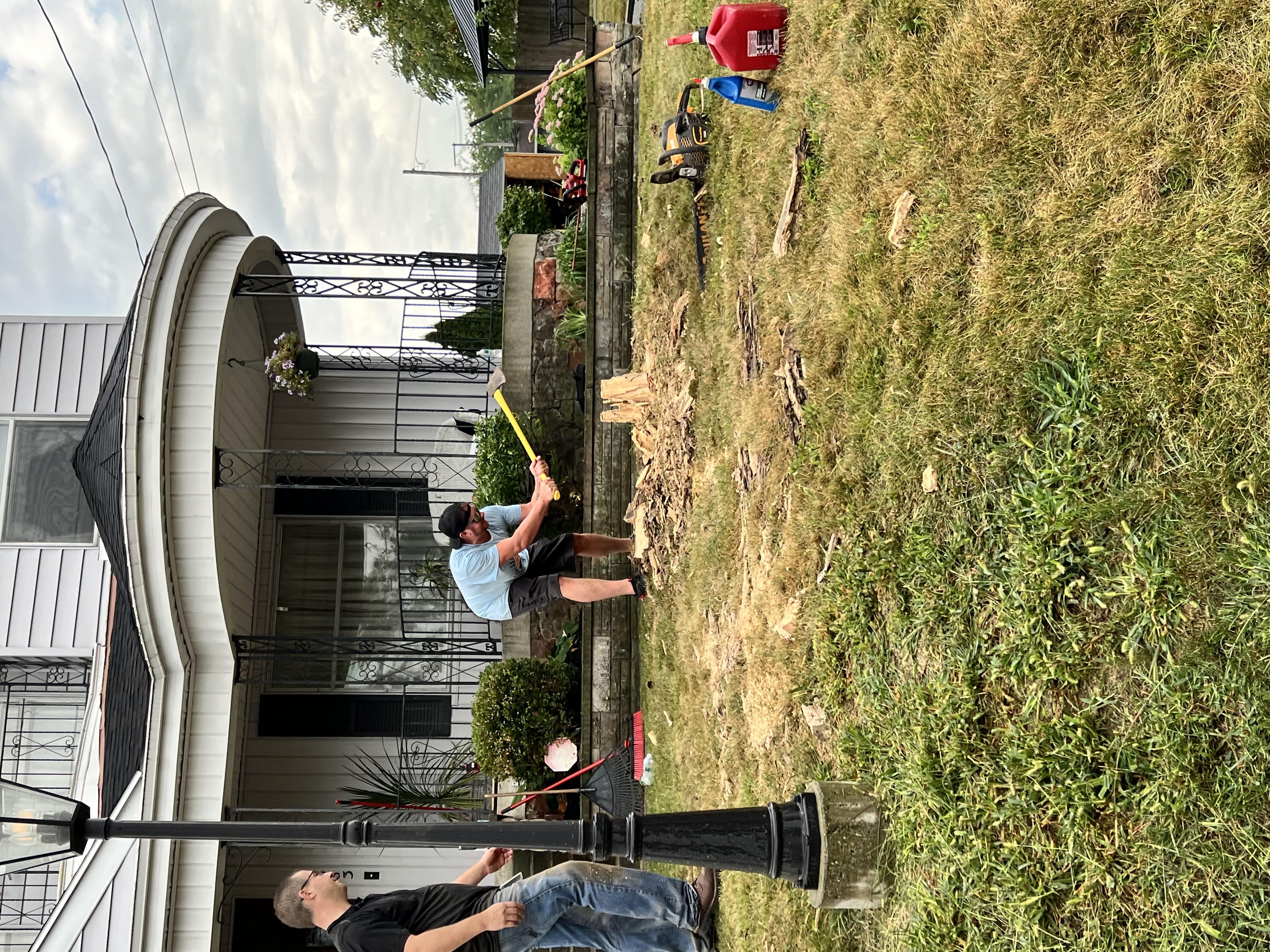 man choping down a tree stump in front of a white house