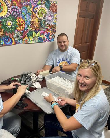 Three people sharpening a bucket of pencils with an electric sharpener