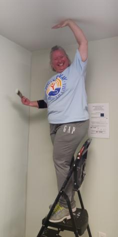 Lady on latter painting a wall with hand on ceiling